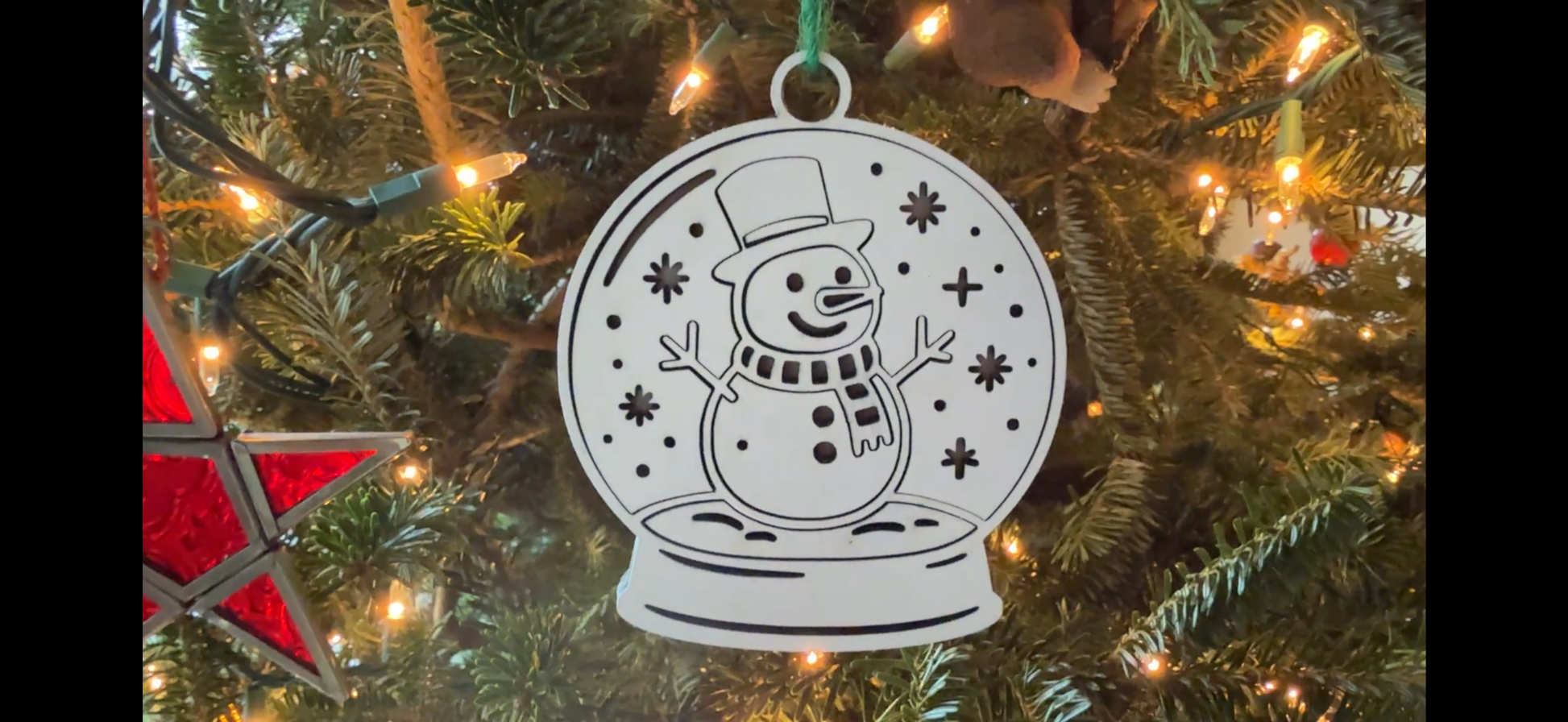 White snow globe ornament with a snowman design on a Christmas tree.