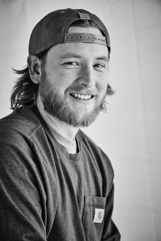 Black and white photo of Nick Leonard, Owner of Statedwoods Supply and Epoxy Forms Co wearing a cap and a branded shirt.